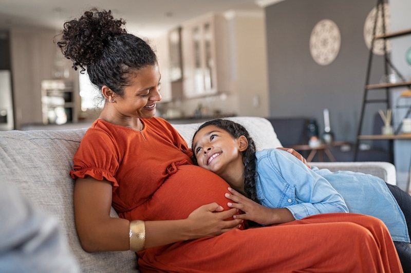 Daughter hugging belly of her expecting mother at home