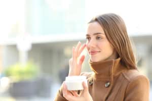 Satisfied woman applying mousturizer cream on her face in winter in the street